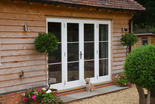 a set of french doors on a cladded building with a dog sat in front