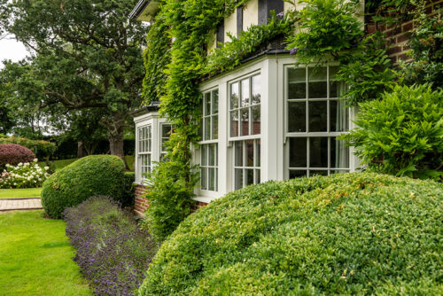 two sash window bays surrounded by greenery and hedges