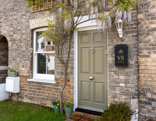an olive coloured front door with a sash window, both underneath blooming wisteria