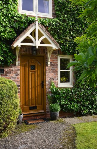 a gothic style door in a dark oak stain, surrounded by ivy and under a stylish canopy