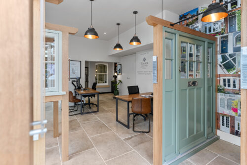 a large green front door with sidelights on display in front of a desk with chairs