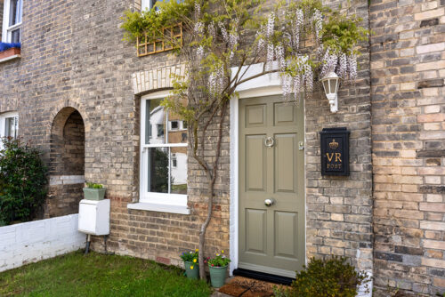 a green solid front door next to a sash window, both surrounded by wisteria