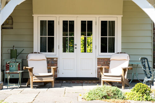 a set of white french doors and casement windows behind a pair of deck chairs