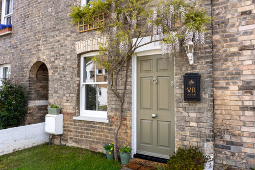 a solid timber front door and white sash window surrounded by wisteria