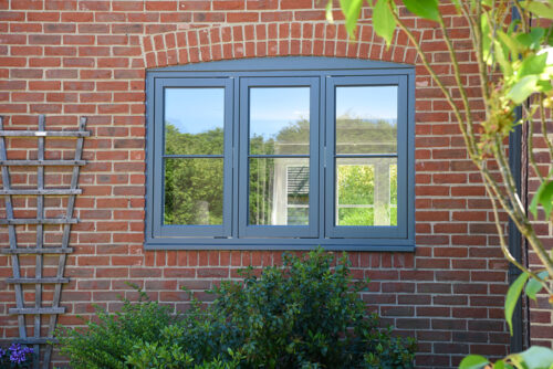 A set of grey casement windows on a red brick home