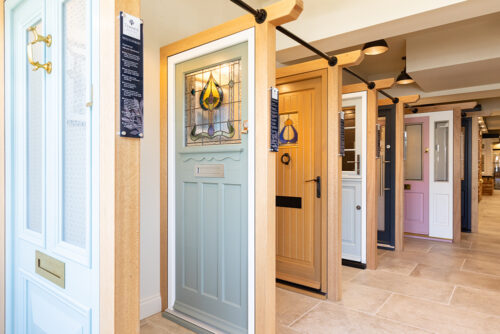 a row of timber front doors, one with stained glass, on display in a showroom