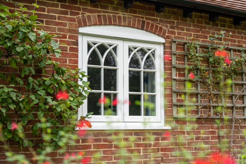a white window with gothic glazing bars on a red brick home