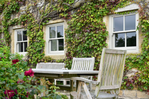 three sash windows on an ivy covered property behind wooden garden furniture