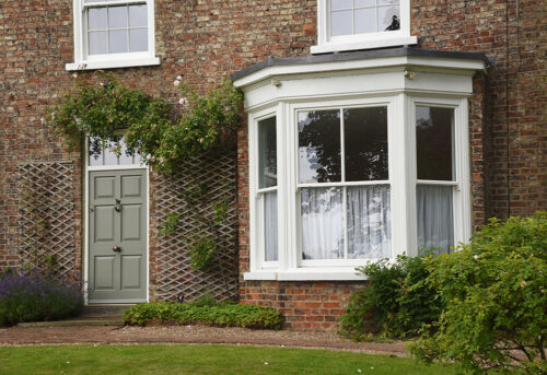 a large sash bay window next to a green solid front door