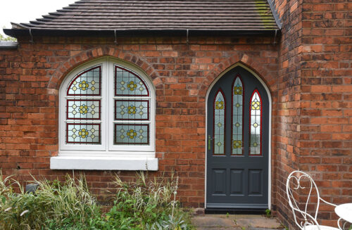 an arched gothic front door and casement window, both featuring floral styled stained glass