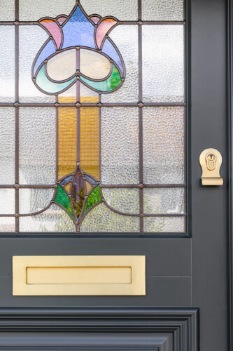 a dark front door with a brass letterbox and escutcheon, and bespoke stained glass