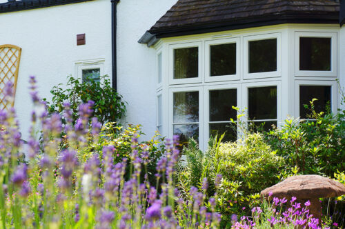 white casement bay window set behind a beautiful blooming garden