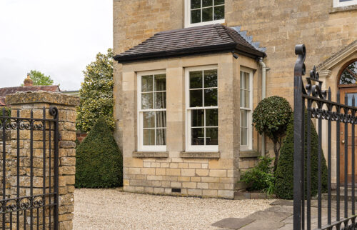a stone property beyond a set of open gates, with white sash windows