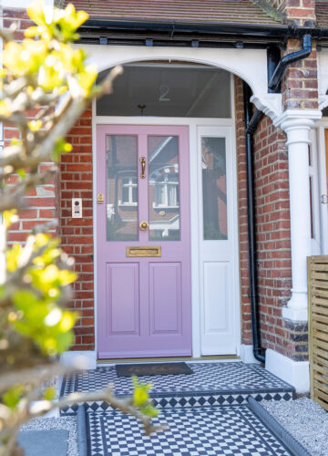 a pink victorian style front door at the end of a path with black and white chequered tiles