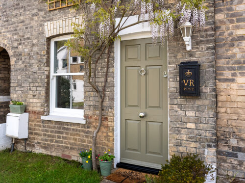 a townhouse with a solid timber front door and white sash window, both surrounded by wisteria